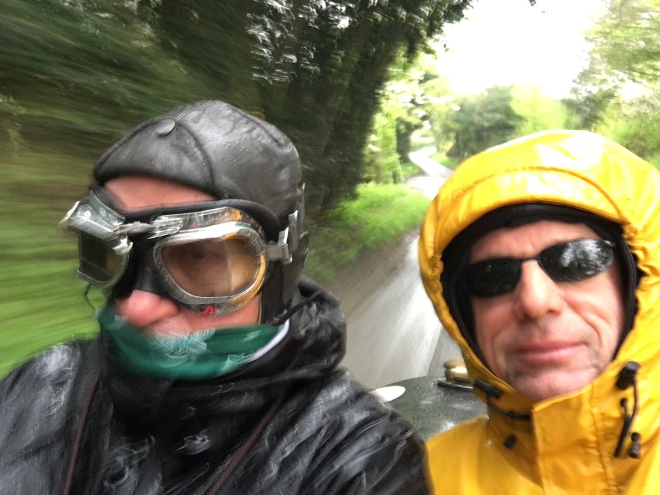 Bill Hoff stands in a bright yellow racing suit under heavy rain, with the historic Brooklands racetrack behind him. Raindrops shine on his gear, showing his excitement for the race.