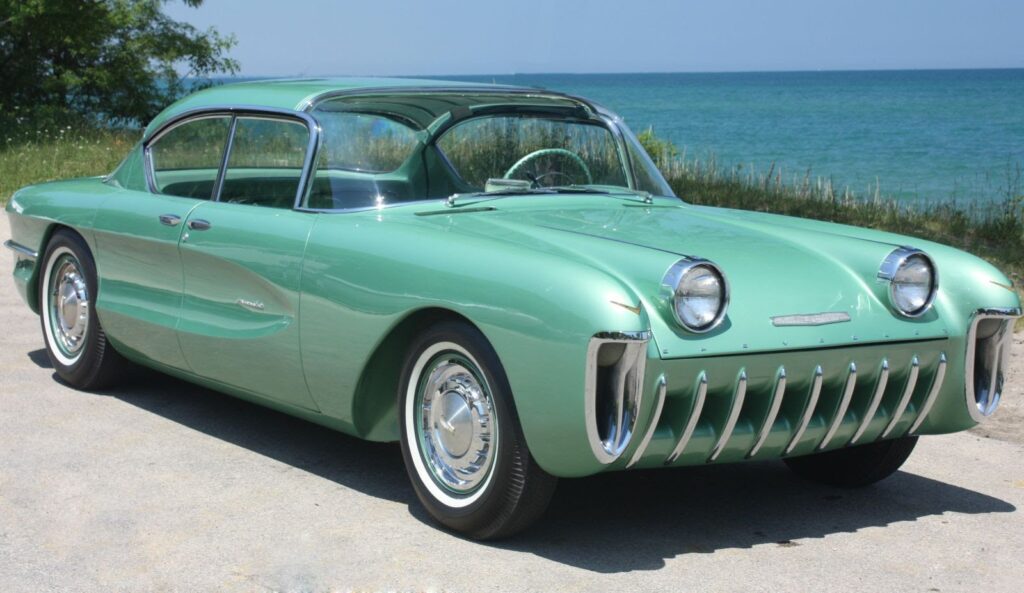 Check out this stunning 1950s Packard Predictor concept car in seafoam green by the lakeside. Explore more vintage car stories on TheSteeringColumn by Darrel Burnett. (138 characters)