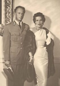 King Leopold III and Princess Lilian stand together, dressed in elegant attire, exuding royal grace against a backdrop of a grand palace interior.